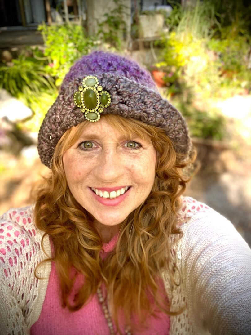 A woman with long red hair wearing a purple hat.