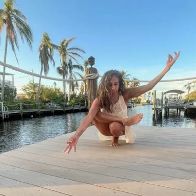 A woman is squatting on the dock by the water.