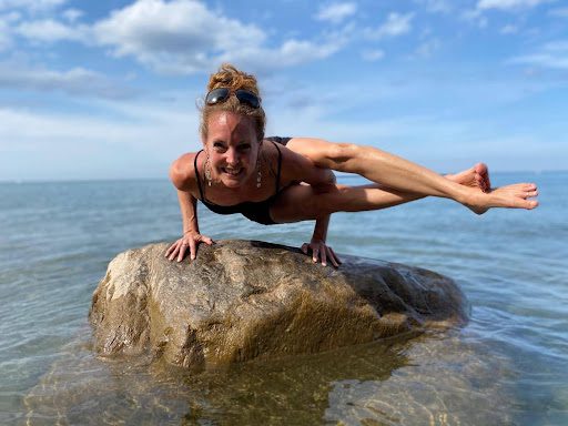 A woman is doing a handstand on a rock in the water.