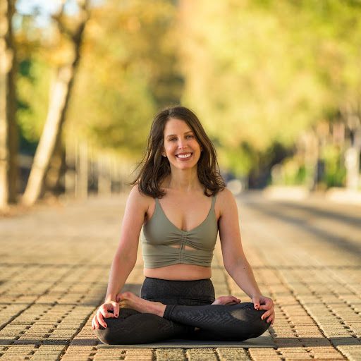 A woman sitting on the ground in a yoga pose.