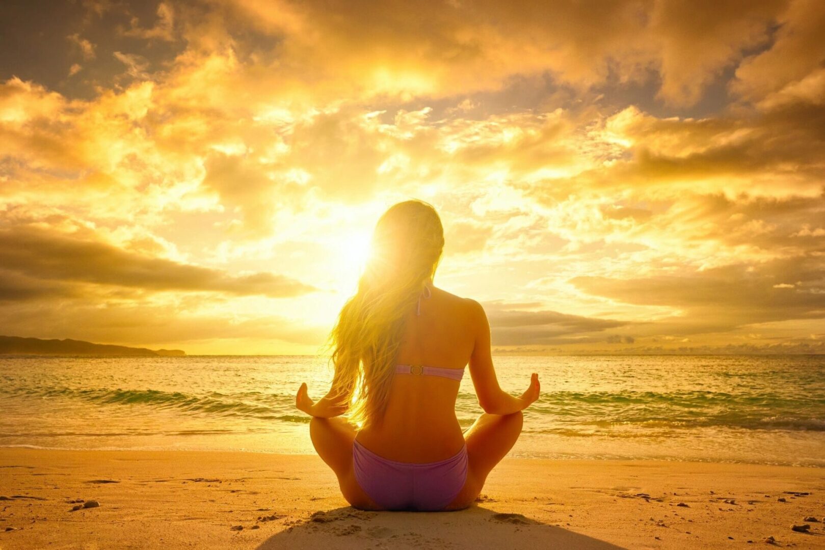 Woman meditating on beach at sunset.