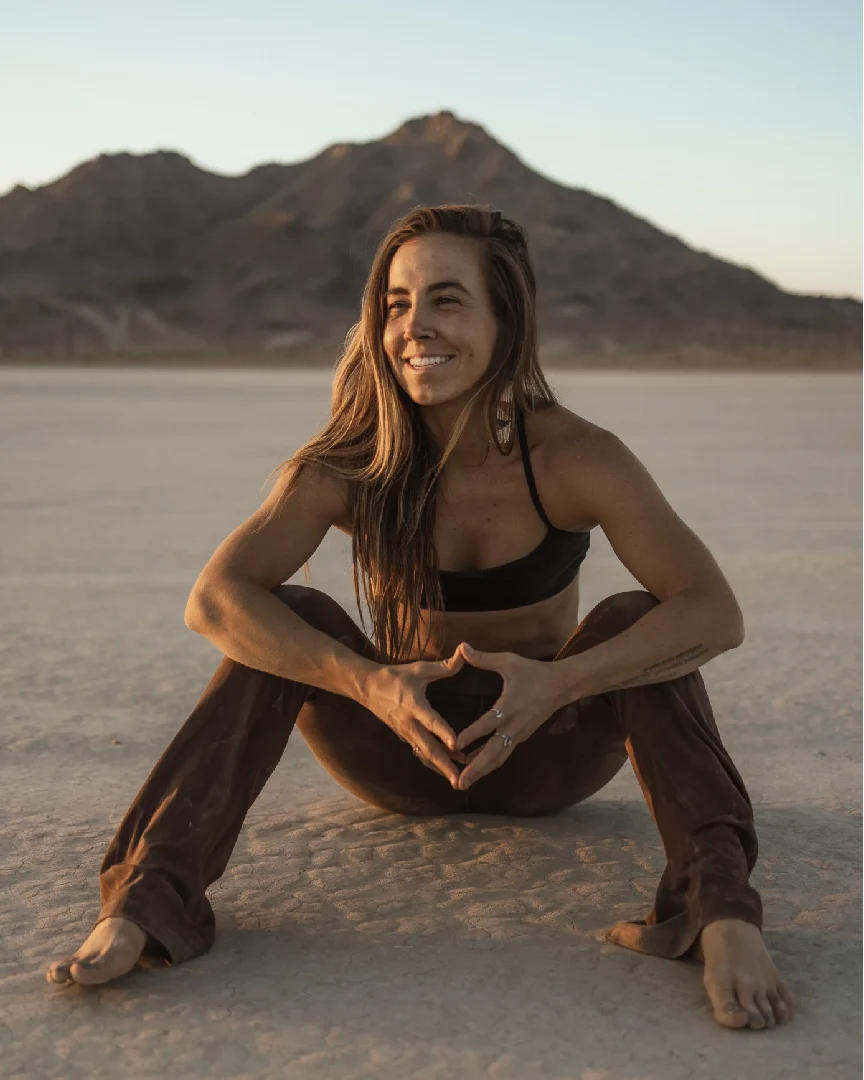 Smiling woman in brown pants, desert landscape.