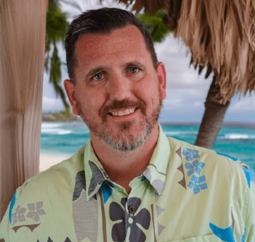 Man in Hawaiian shirt smiling on beach.