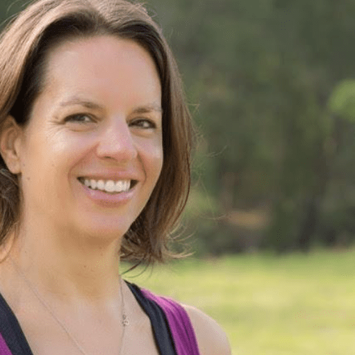 A woman smiling for the camera in front of some grass.