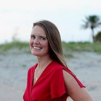 A woman in red shirt standing on beach.