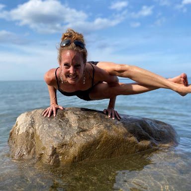 A woman is doing a handstand on a rock in the water.